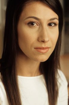 Intimate portrait of a brunette woman with a serene expression, bathed in warm indoor lighting.