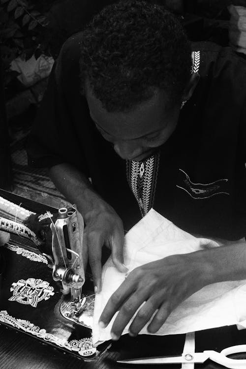 Grayscale Photo of Man Using a Sewing Machine