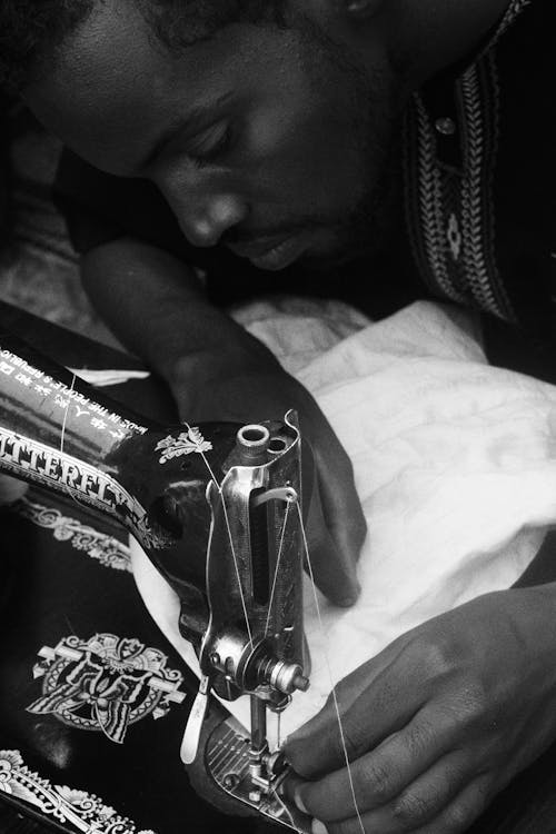 A Grayscale Photo of a Man Using a Sewing Machine