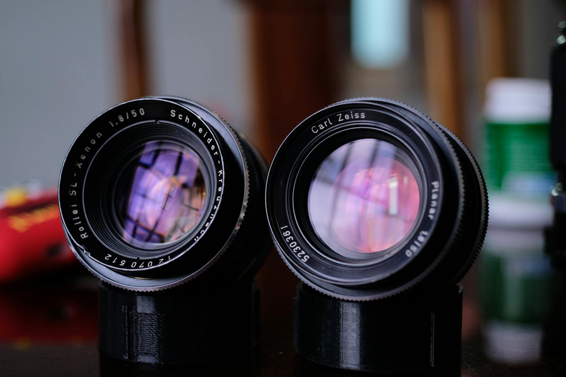Two vintage camera lenses, Schneider Kreuznach and Carl Zeiss, reflecting vibrant colors.