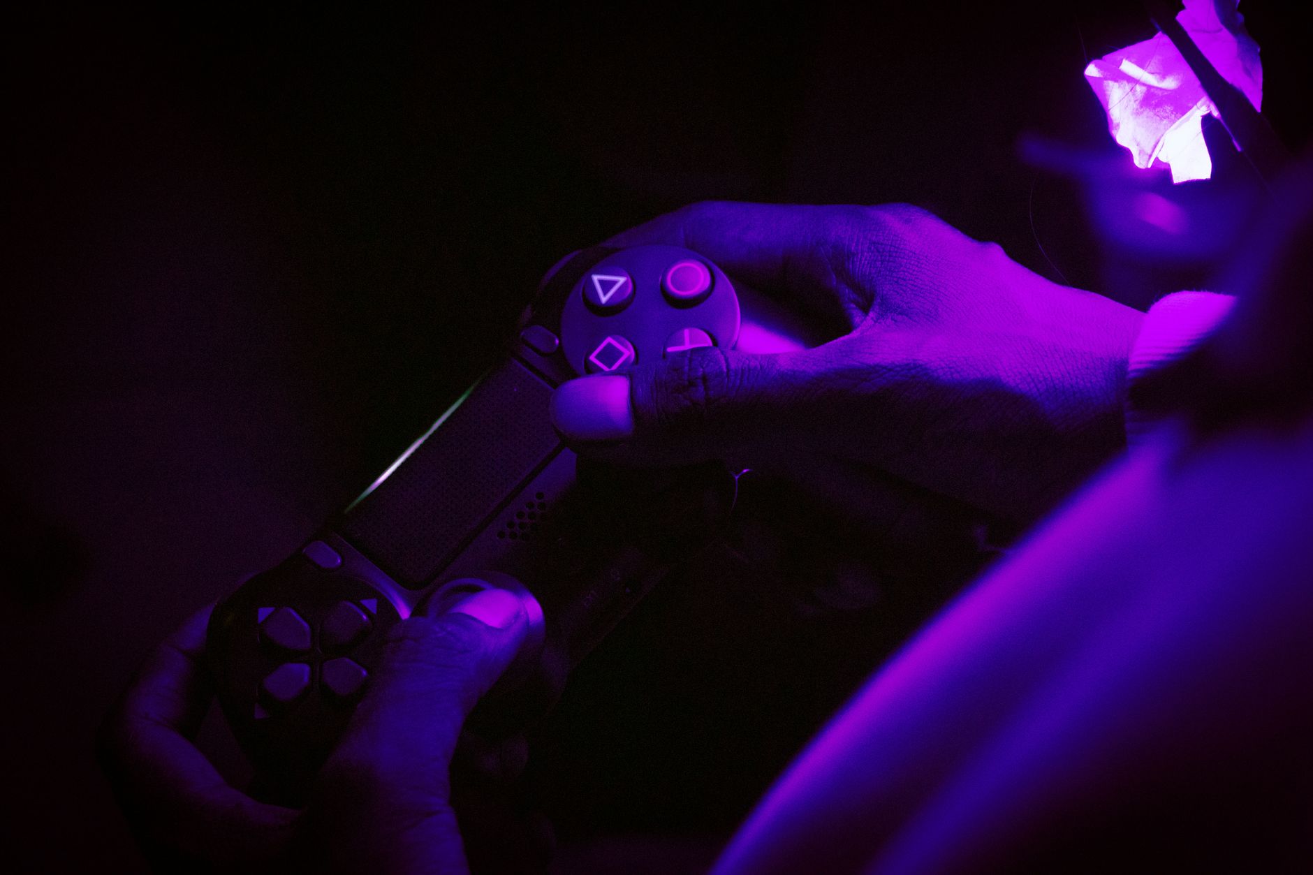 A close-up shot of hands gripping a gaming controller, illuminated by purple light, creating a vibrant atmosphere.