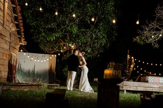 A couple kisses under string lights at an outdoor wedding venue at night.