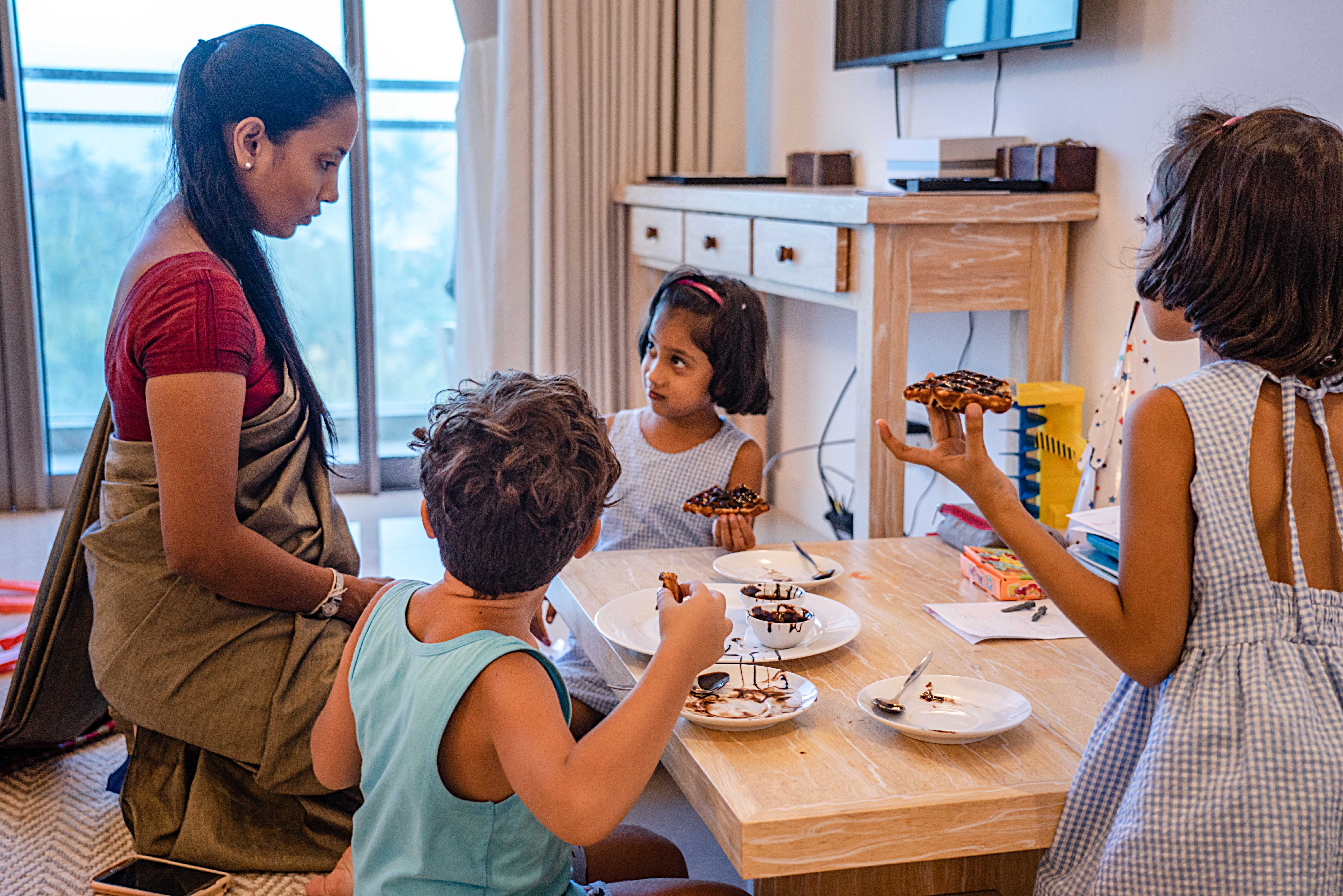 Mother and children bonding over waffles at home, enjoying dessert time together indoors.