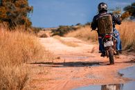 A motorcyclist navigates a dirt road through rural Zimbabwe, showcasing adventure and exploration.