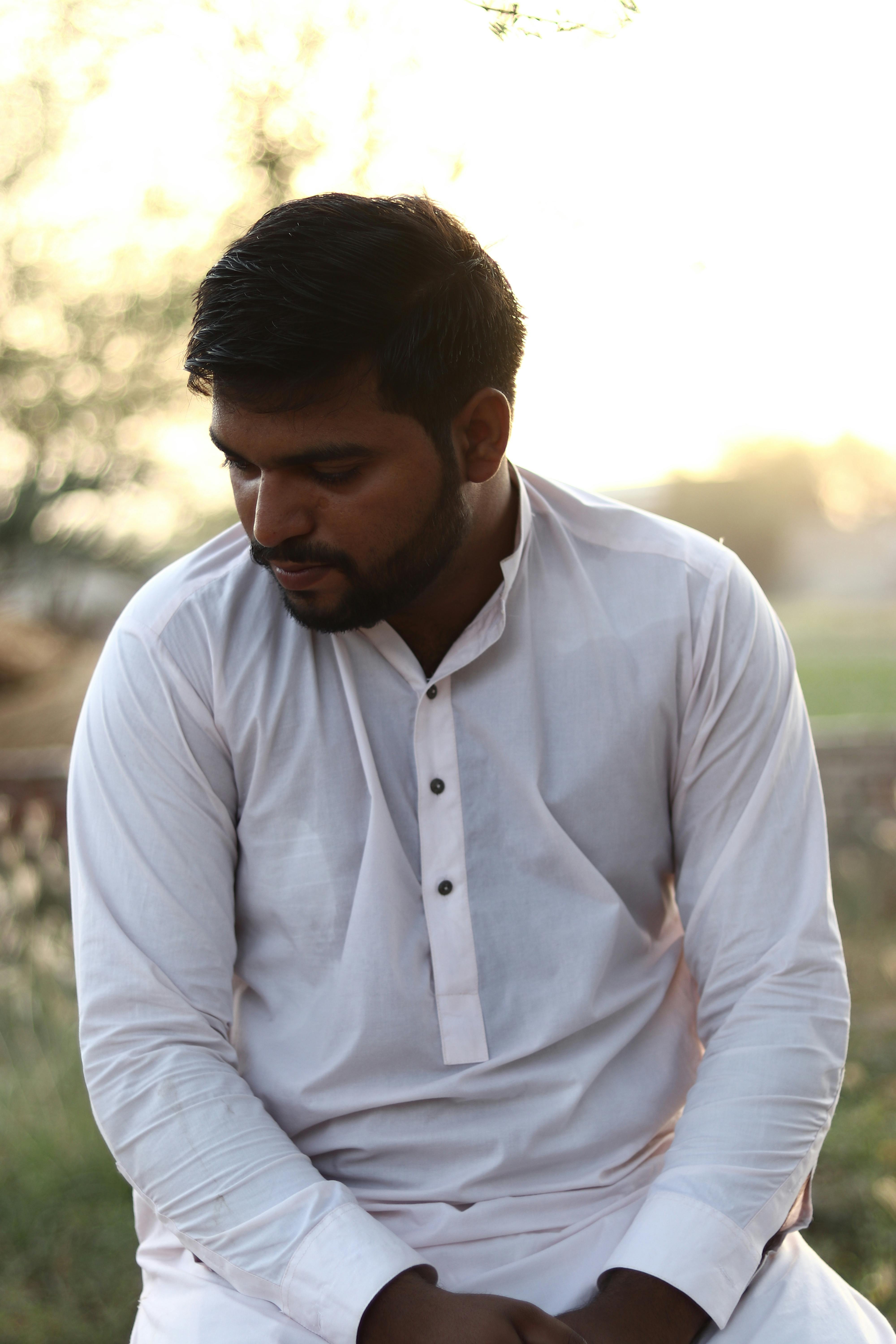 A thoughtful man in a traditional white kurta sitting outdoors during sunset.