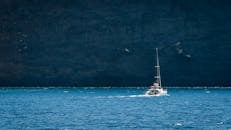 一艘帆船航行在广阔的蓝色海水中，驶向圣托里尼雄伟的悬崖