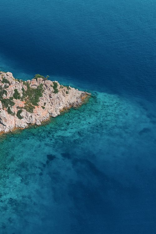 Free Stunning aerial shot of a rocky coastline surrounded by vibrant blue waters, showcasing nature's beauty. Stock Photo