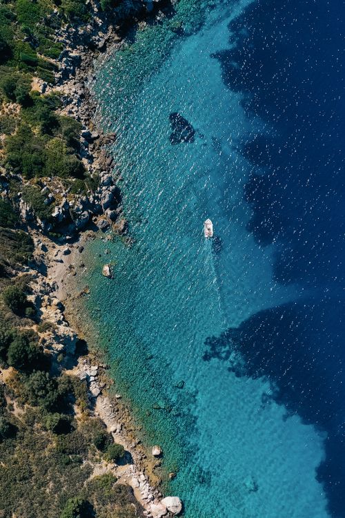 Free Stunning aerial shot capturing a boat navigating crystal-clear azure waters along a rocky coastline. Stock Photo