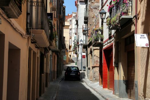 Explore a picturesque alley with rustic architecture and vibrant balconies in Falset, Spain.