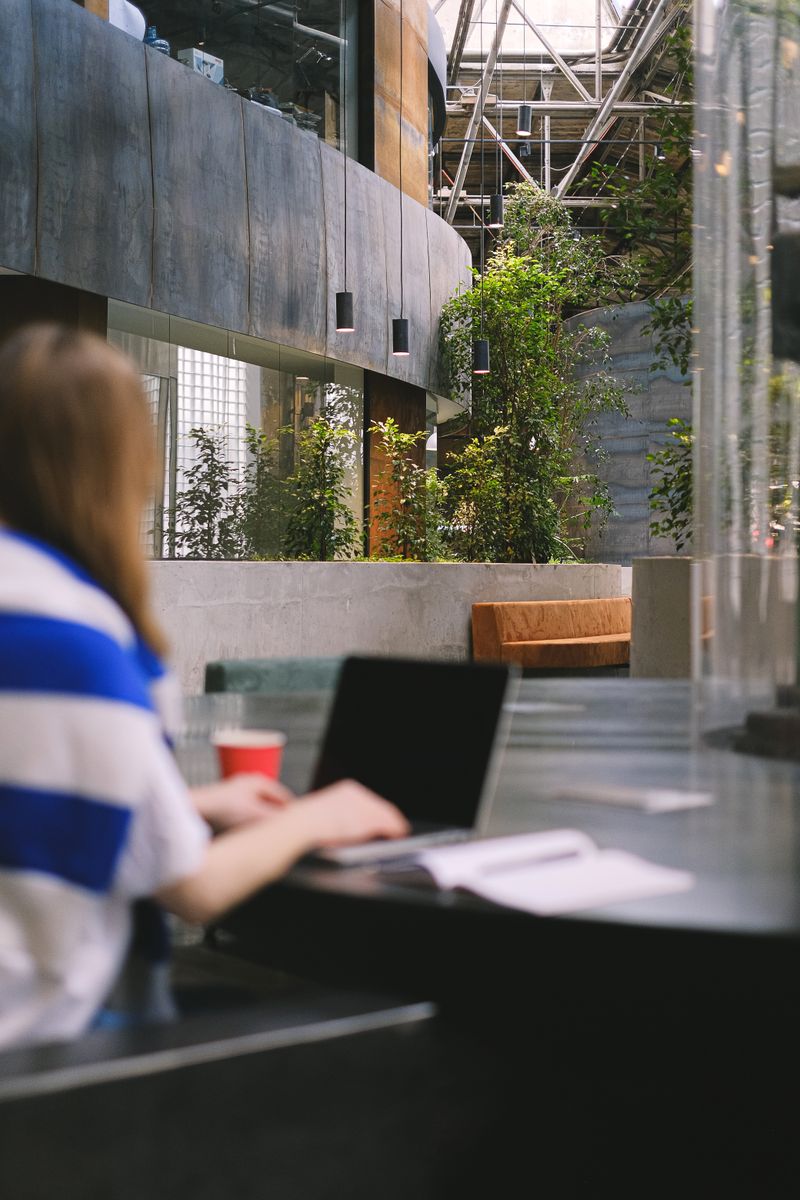 Young woman studying on a laptop in a modern campus atrium with industrial design elements.