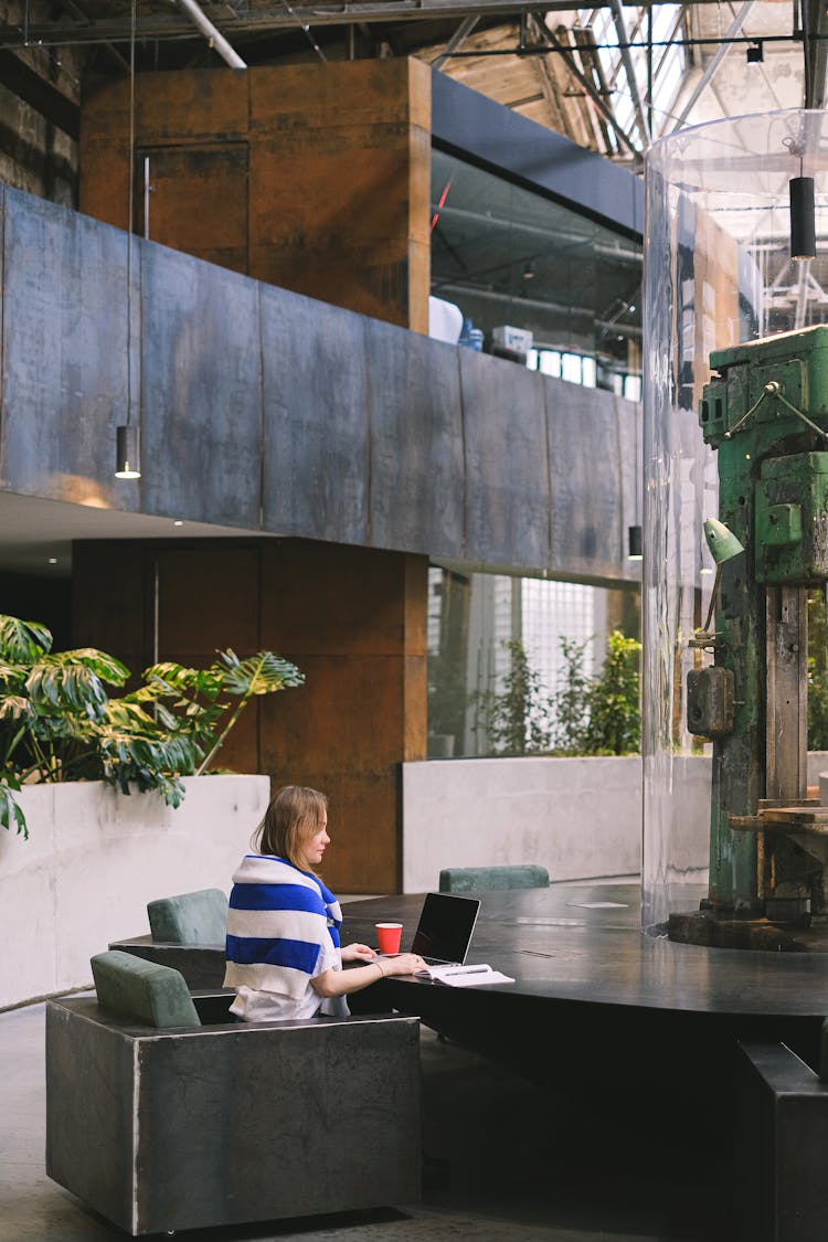 Woman Working On A Laptop At A Table With A Decorative Sculpture In The Middle