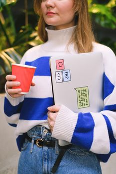 Fashionable woman in striped sweater holding a laptop and coffee cup, creating a modern lifestyle vibe.