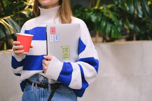 Woman in Striped Sweater Holding Laptop and Paper Cup