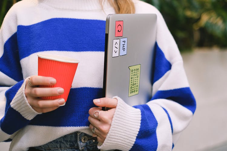 A Person Holding A Laptop And Drink