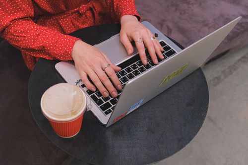 Free A woman in a red polka dot dress typing on a laptop with coffee nearby. Stock Photo