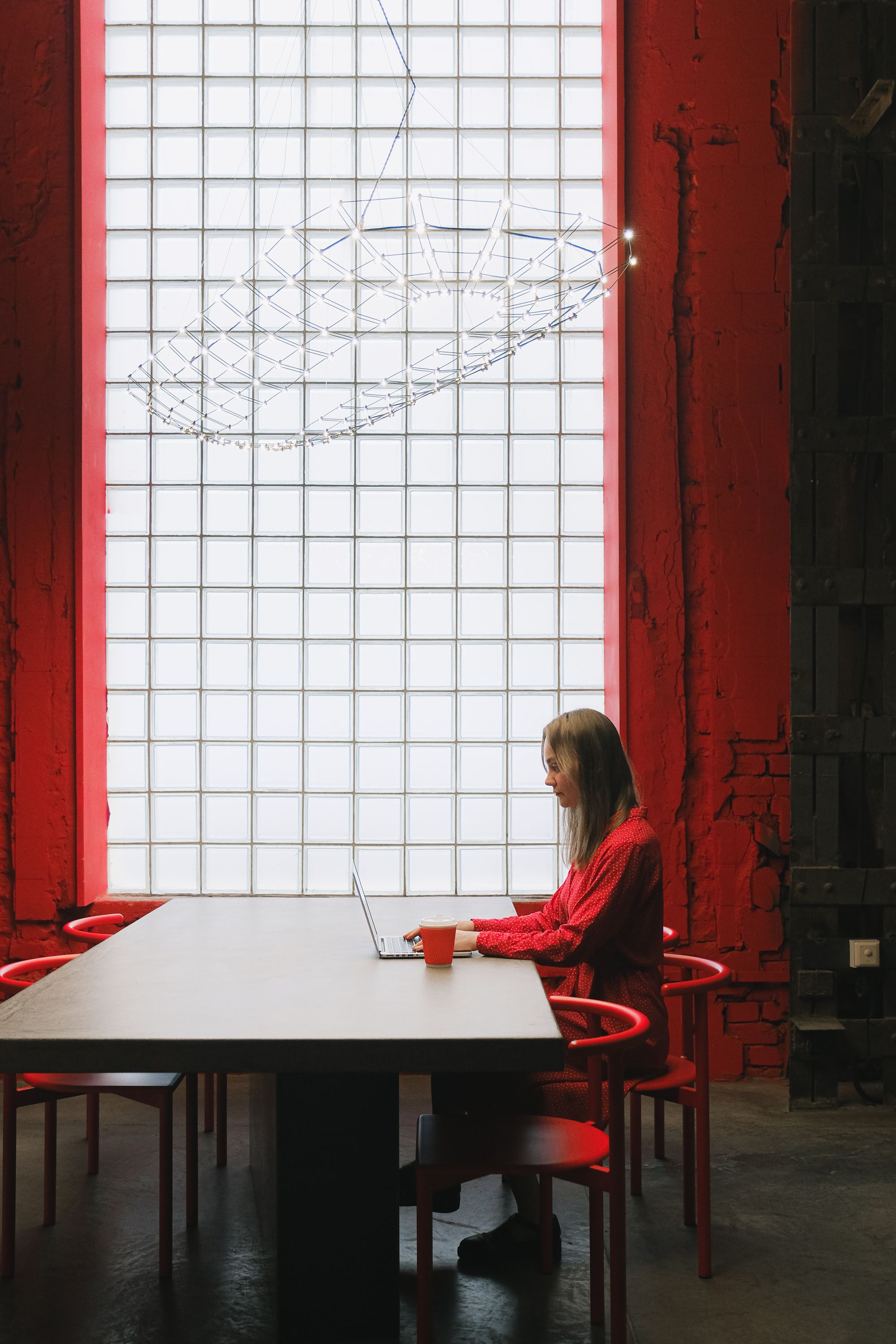 A designer working at a long desk in a studio with red walls and glass-block windows