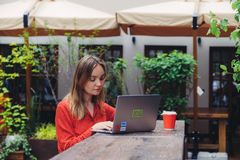 Young woman working on a laptop in an outdoor cafe setting, enjoying a cup of coffee.