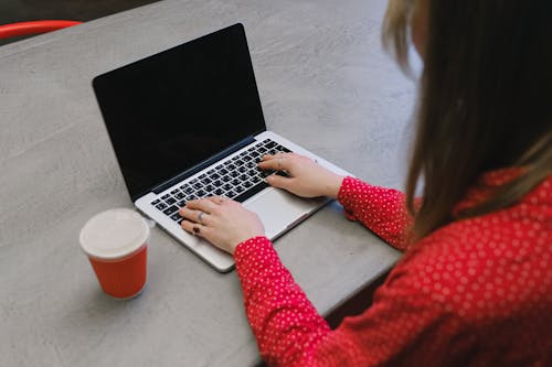 A Woman in Red Long Sleeves Typing on Her Laptop