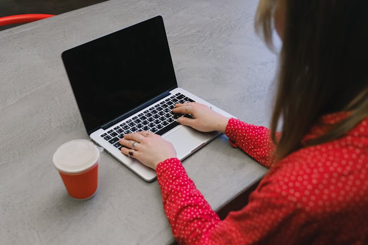 A Woman In Red Long Sleeves Typing On Her Laptop