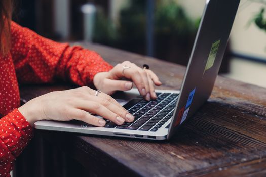 Close-up of hands typing on a laptop placed on a wooden table outdoors.