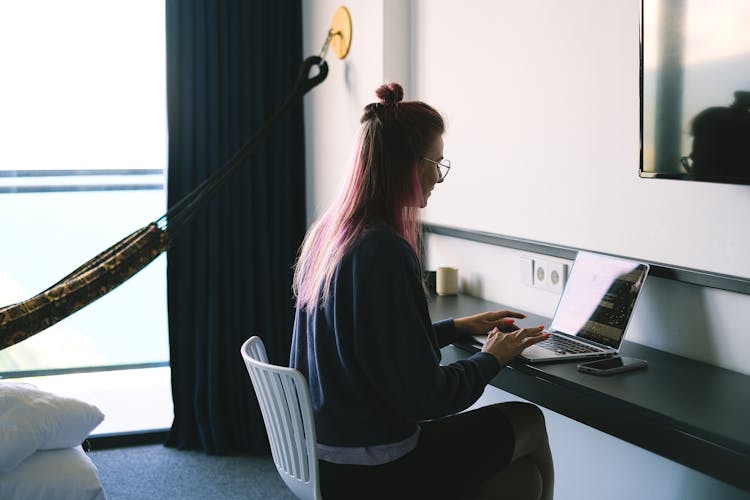 Woman Working On Laptop By Long Desk In Room