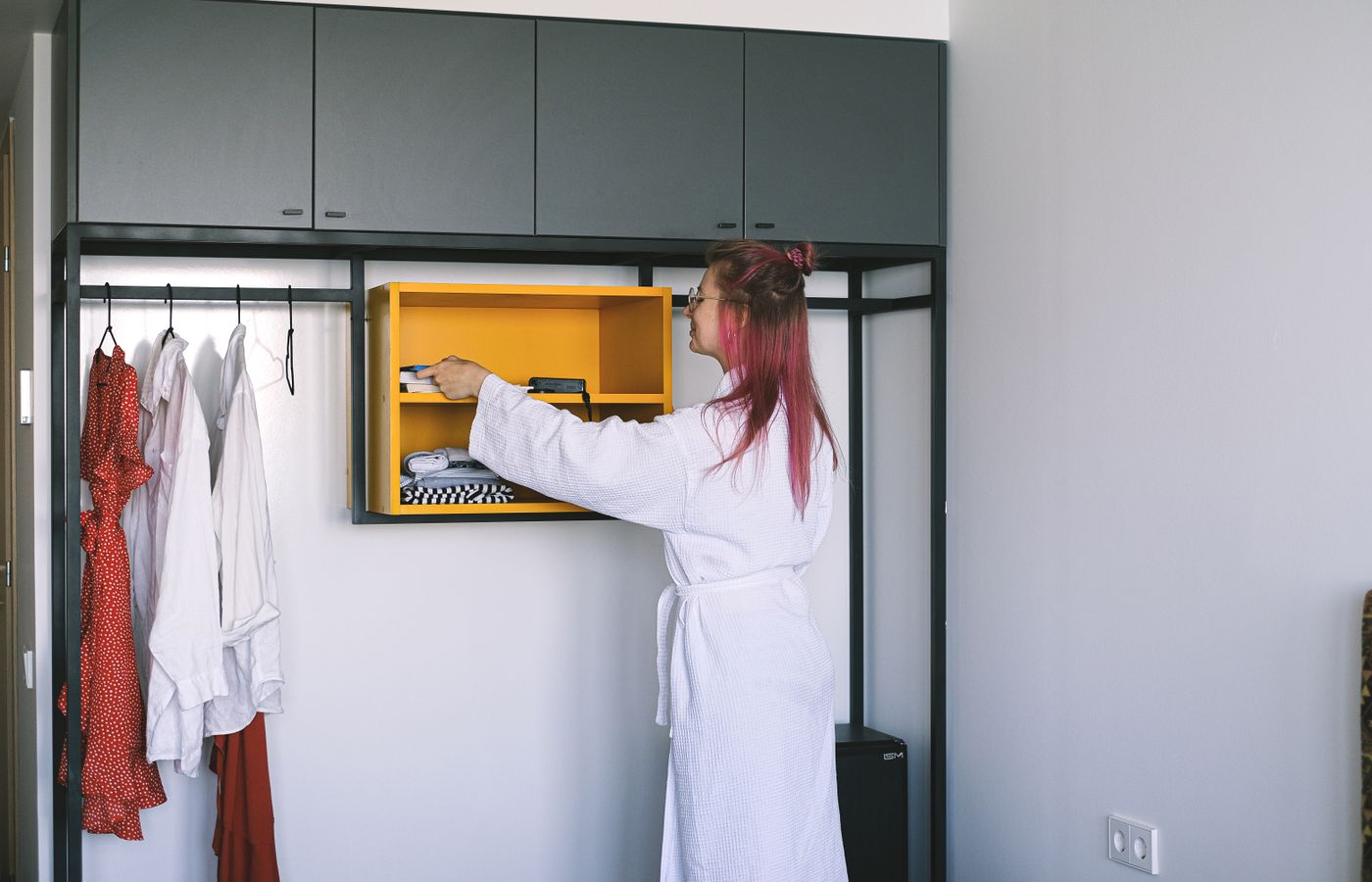 A woman in a bathrobe organizes a wardrobe in a modern hotel room.