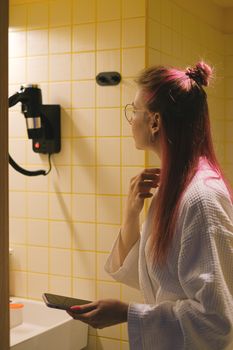 Woman in a hotel bathroom looking at herself with a smartphone and hairdryer.