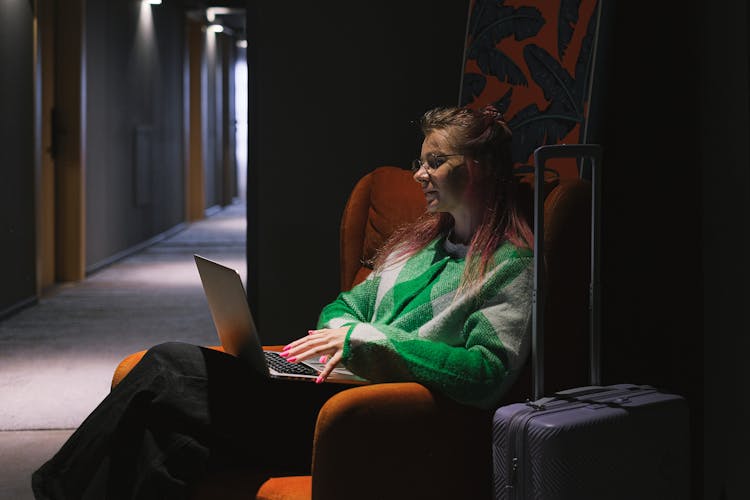 Woman Sitting In Corner Of Hotel Hallway Working On Laptop