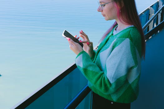 Woman using a smartphone on a balcony with a tranquil ocean view.