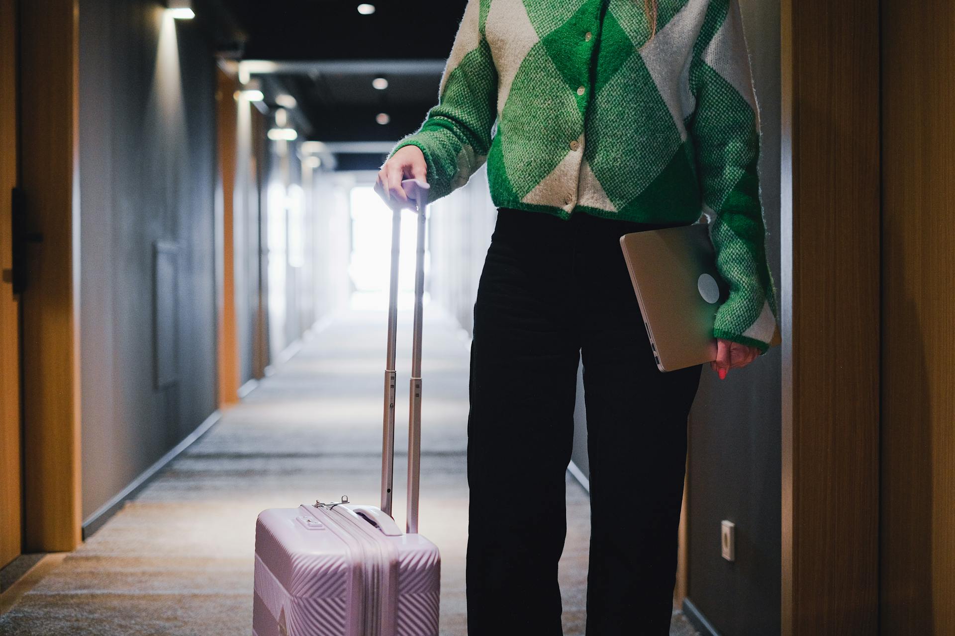 A person in a hotel corridor holding luggage and a laptop, showcasing travel and business.