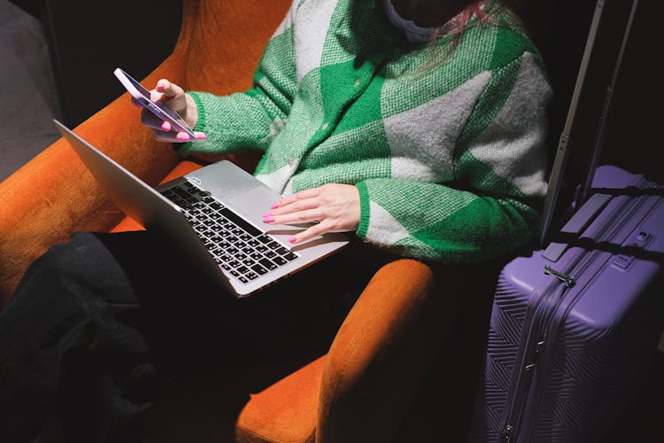 A Woman Using A Smartphone And A Laptop While Sitting On An Armchair