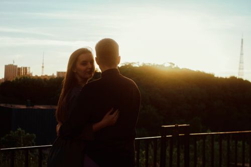 Free Couple embracing outdoors at sunset with cityscape in the background. Stock Photo