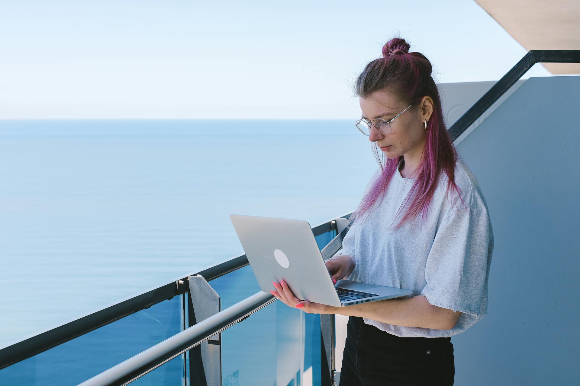 A young woman works remotely on her laptop by the sea on a sunny day, embodying the digital nomad lifestyle.