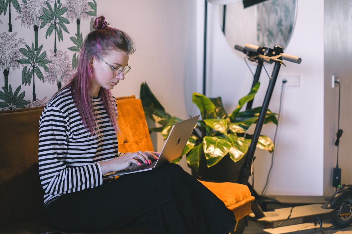 Free A Woman in a Striped Shirt Typing on a Laptop Stock Photo