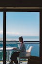 年轻女性自由职业者在阳光明媚的日子里，在阳台上使用笔记本电脑，可以看到美丽的海景