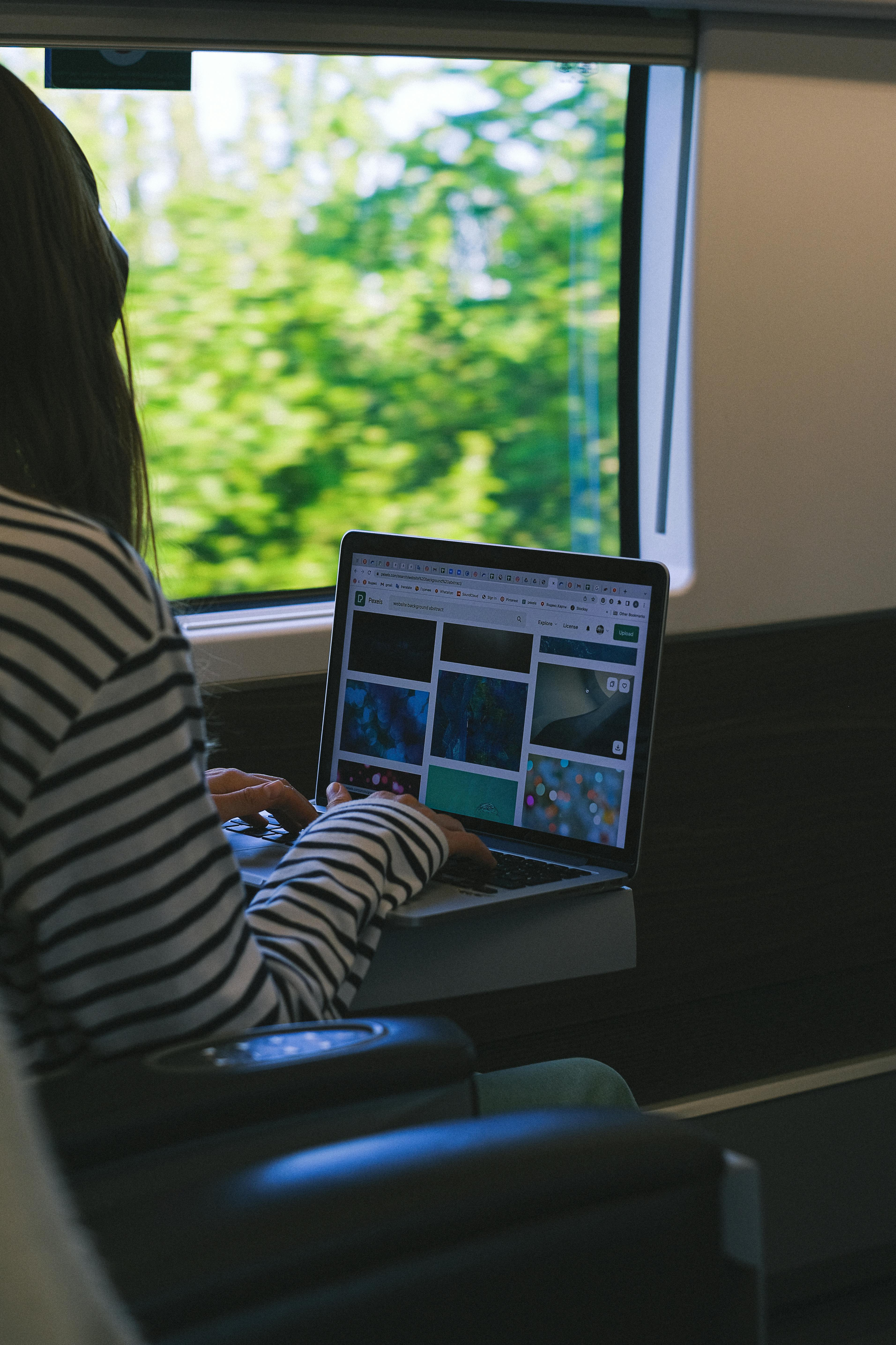 A woman working on a laptop inside a train, overlooking a scenic view.