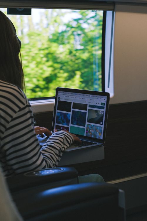 Free A woman working on a laptop inside a train, overlooking a scenic view. Stock Photo