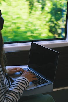A woman typing on a laptop while traveling on a train, capturing the essence of mobile work lifestyle.