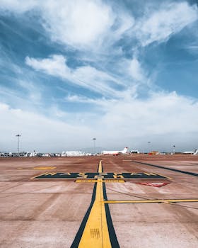 Wide view of an empty airport tarmac with a plane in the distance under a cloudy sky.