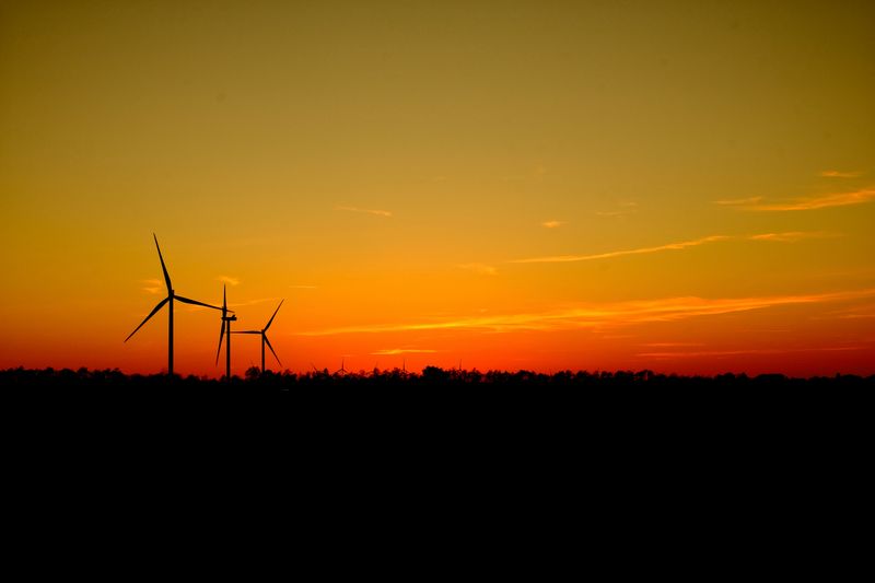 Wind turbines silhouetted against an orange evening sky — photo by Phong Thanh on Pexels