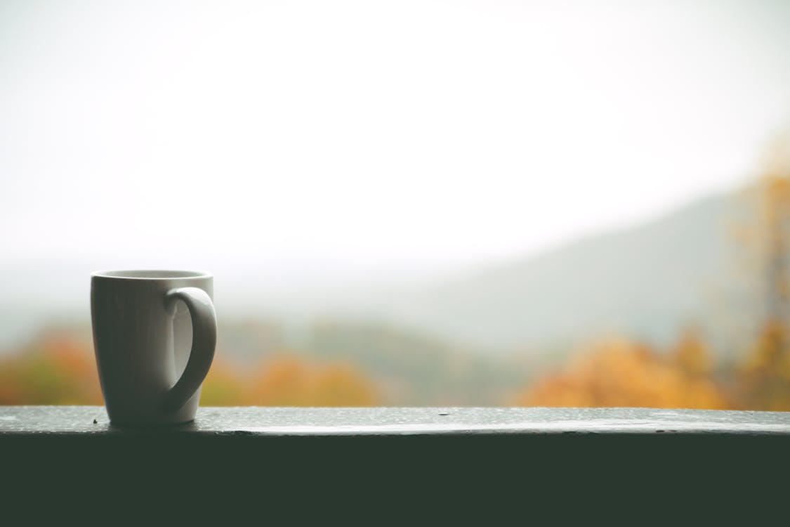 White Mug on Window over Looking Autumn Trees and Hills in Distance during Daytime