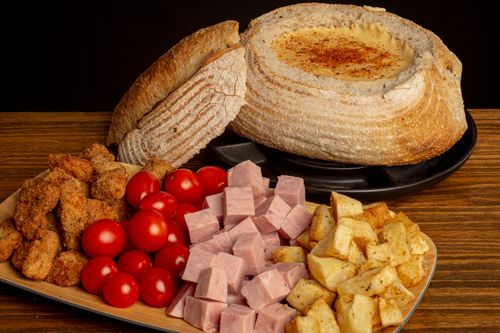 Free Delicious rustic bread bowl filled with cheese, surrounded by deli meats and fresh vegetables. Stock Photo