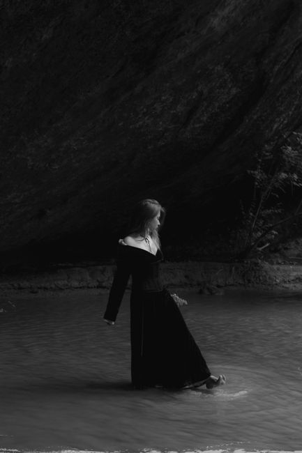 Black and white portrait of a barefoot woman standing in water, evoking a serene and contemplative mood.