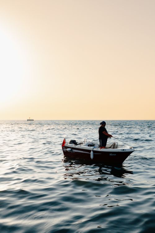 Free A man stands fishing on a boat during a serene sunset over the sea in Yalova, Turkey. Ideal for tranquil and nautical themes. Stock Photo