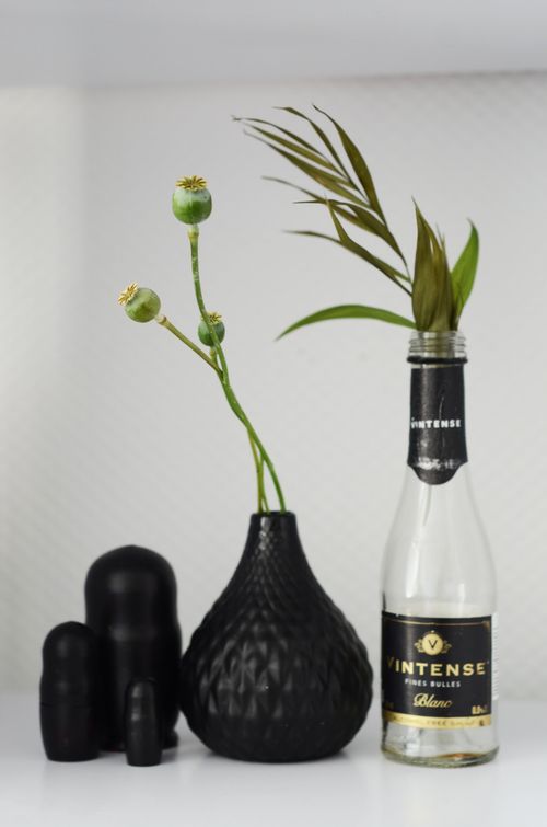 Free Elegant display of a black vase with stems and a Vintense bottle on a white background. Stock Photo