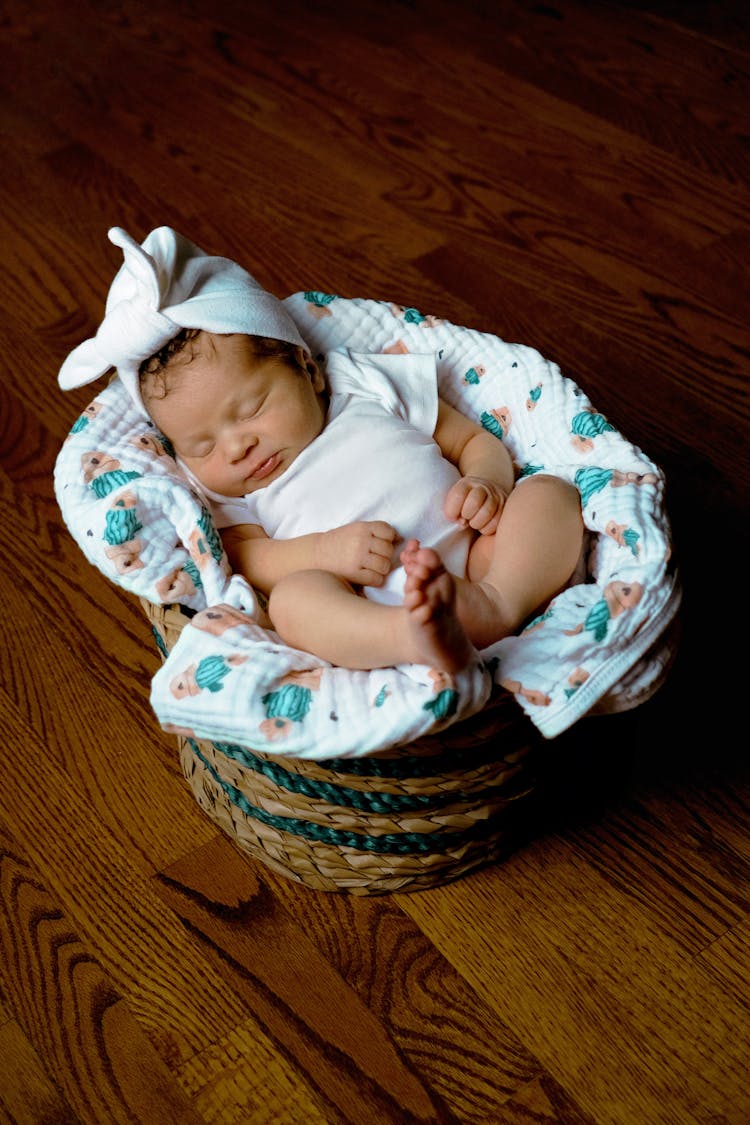 A Baby In White Onesie Lying On White Textile In A Basket