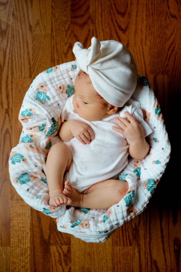 A Baby In White Onesie Lying On White Textile