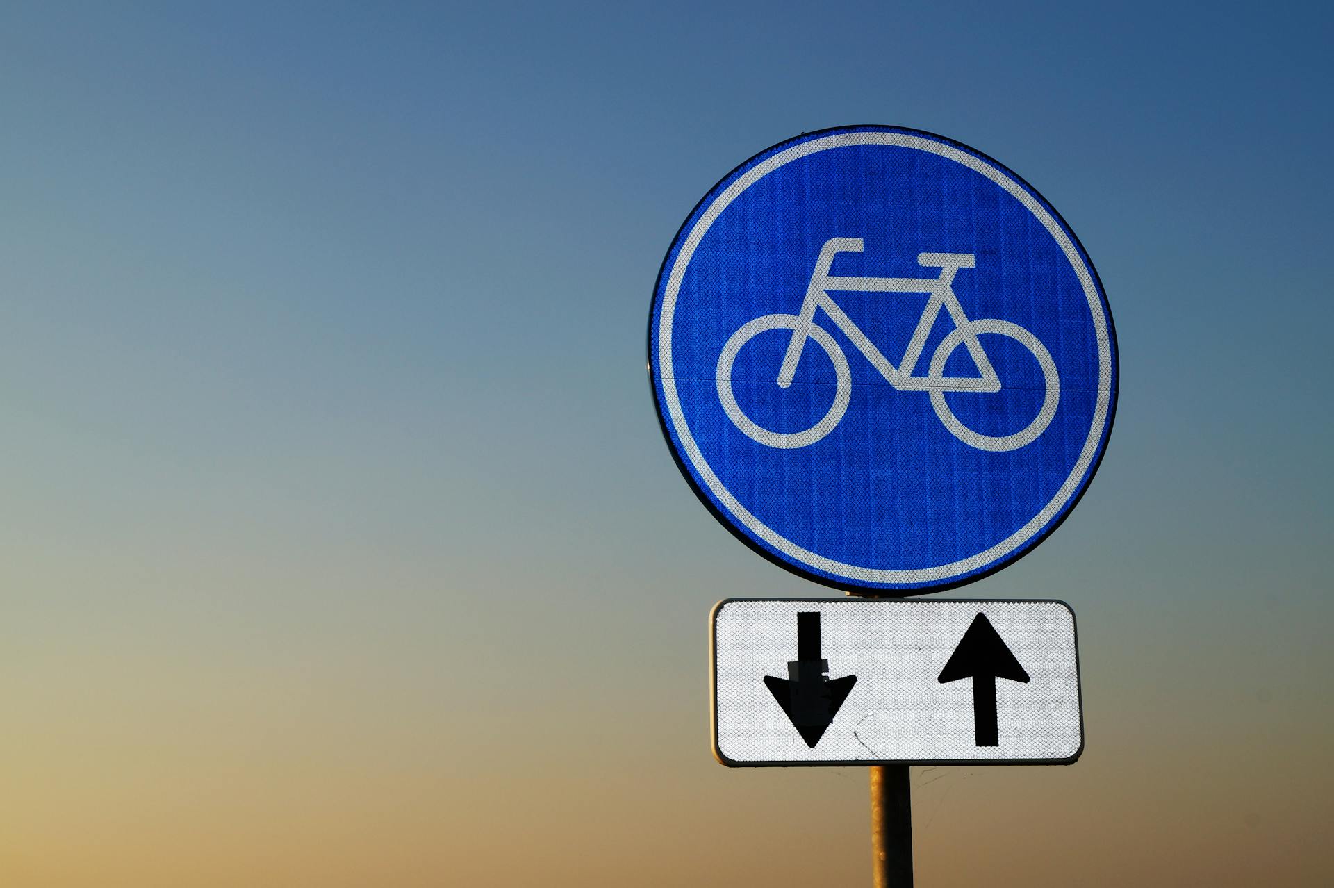 Bicycle route sign with directional arrows against a twilight sky, symbolizing travel guidance.