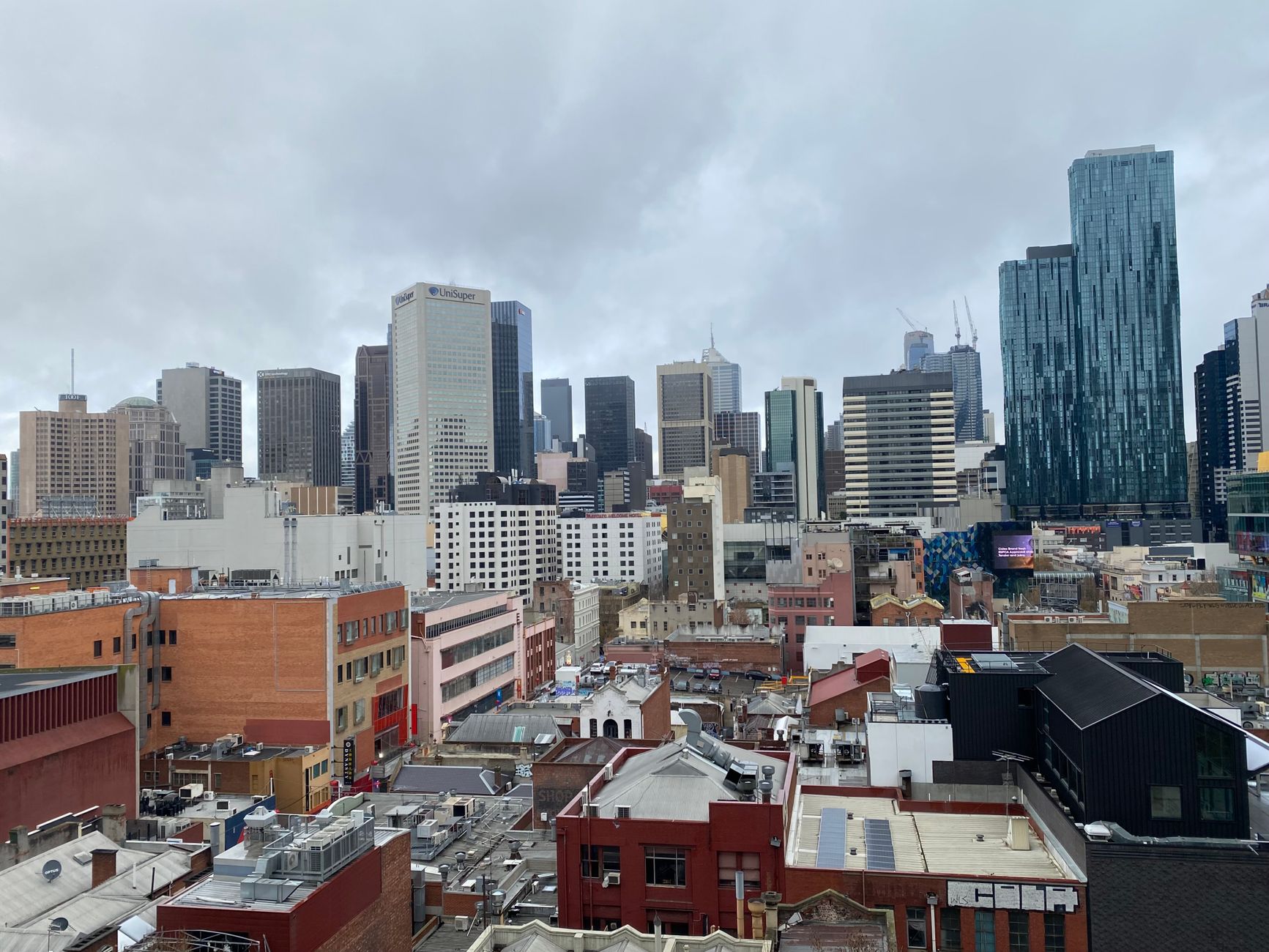 Aerial view of Melbourne's skyline under cloudy skies, showcasing modern architecture and urban life.