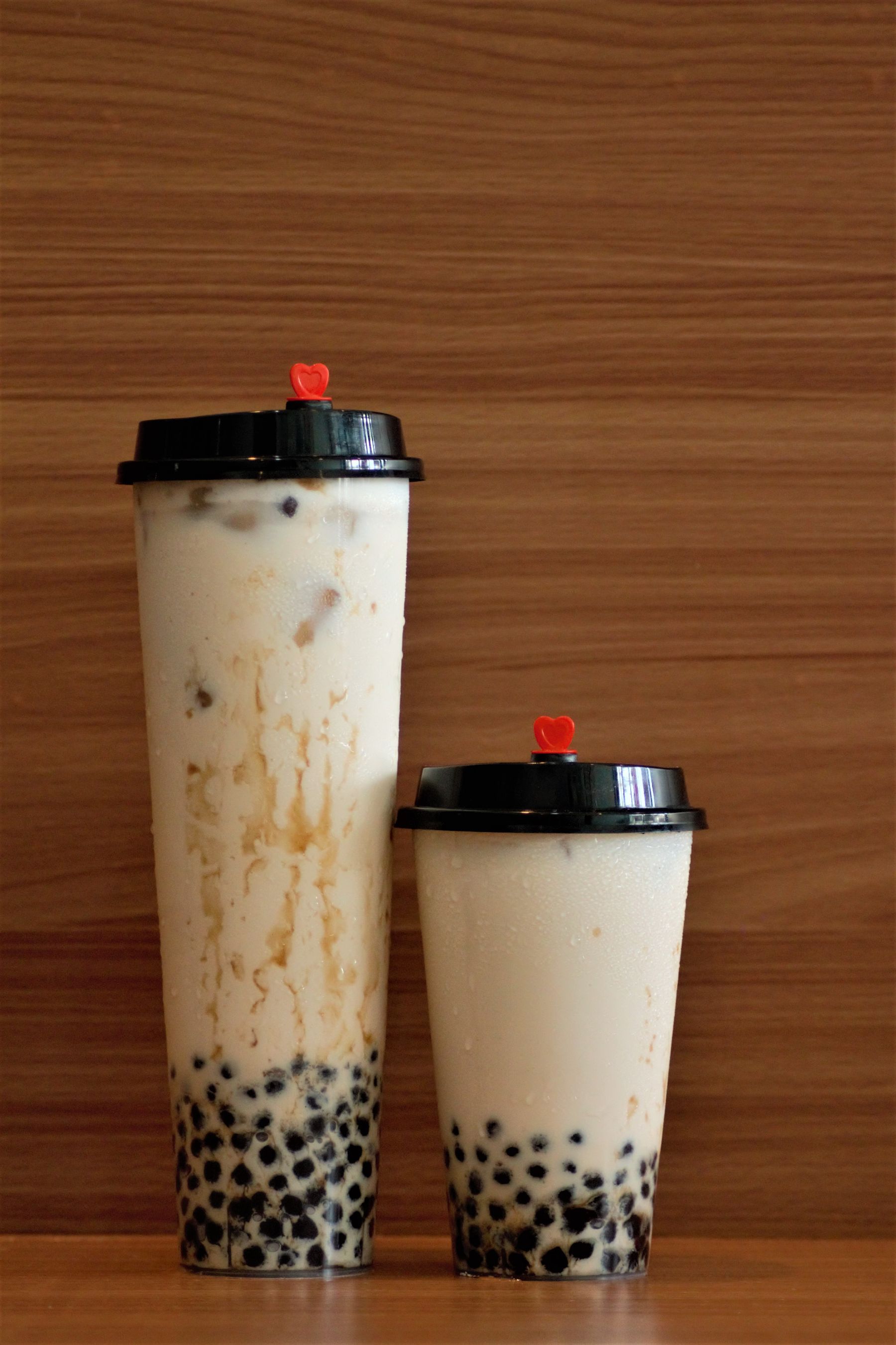 Two logo-free milk tea cups with tapioca pearls against a wooden backdrop